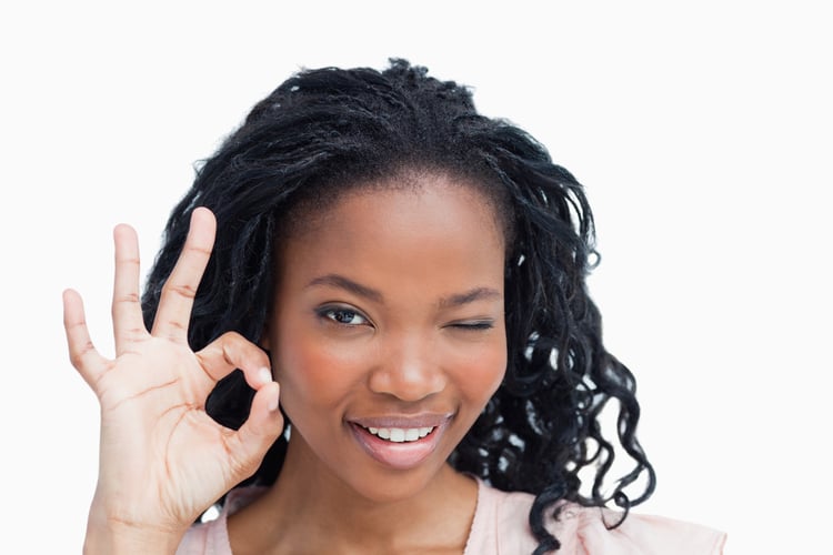 A young woman is winking and holding her hand in the okay sign against a white background